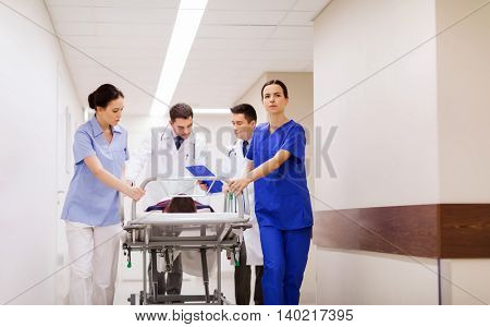 profession, people, health care, reanimation and medicine concept - group of medics or doctors carrying unconscious woman patient on hospital gurney to emergency