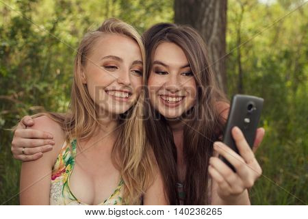 Happy Teenage Girls Taking Selfshot Or Selfy Picture Of Themselves With Mobile Phone Outdoors Over G