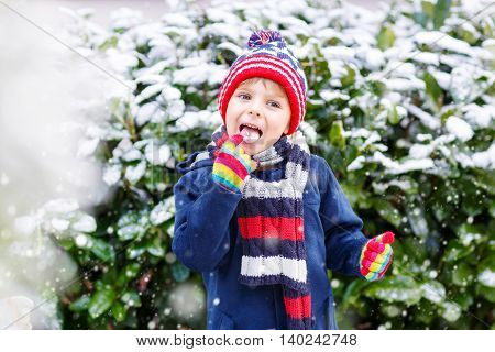 Winter portrait of kid boy in colorful clothes, outdoors during snowfall. Active outoors leisure with children in winter on cold snowy days. Happy child having fun with snow
