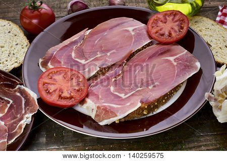 closeup of a plate with spanish pan con tomate y jamon, sliced bread topped with tomato and serrano ham and dressed with olive oil, on a rustic wooden table