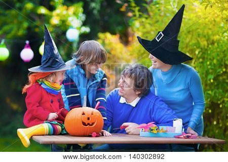 Family carving pumpkin at Halloween. Dressed up child trick or treating. Kids and parents trick or treat. Child in witch costume playing in autumn park. Toddler kid with jack-o-lantern.