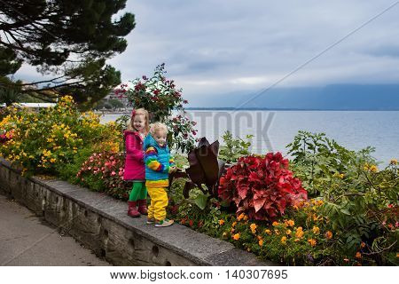 Cute little girl and boy walking down lakeside promenade in Montreux city center on cold autumn day. Children during fall vacation in Switzerland Geneva Lake. Traveling and tourism with kids.