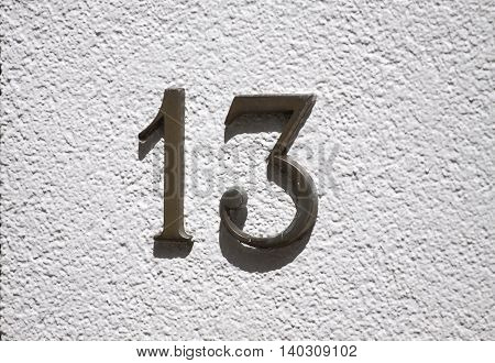Brass house number 13 on a white wall