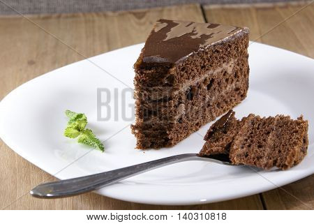 A piece of chocolate cake lying on a white plate on a rustic wooden table