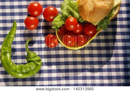 Cozy plaid tablecloth ingredients for a healthy snack on it: whole wheat bun, cheese, tomatoes, lettuce and pepper