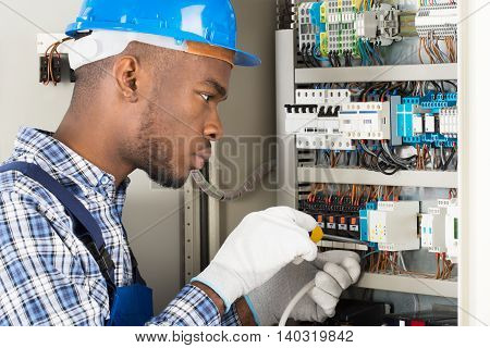 Young African Male Technician Repairing Fusebox With Screwdriver
