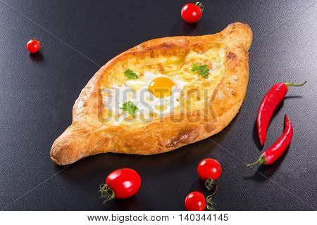 Ajarian khachapuri with egg on black background with cherry tomatoes and red chili pepper authentic recipe view from above close-up