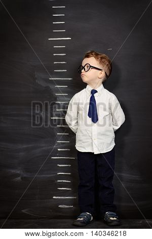Four year old boy in white shirt and a tie standing by a stadiometer, drawn on a blackboard. Education.