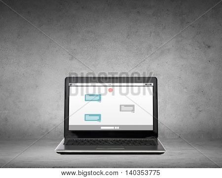 technology, internet and communication online concept - laptop computer with messenger chat on screen over gray concrete background