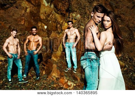 four handsome young macho men with muscular sexy body and six packs on torso in jeans and pretty woman in white dress sunny day outdoor on stony natural background