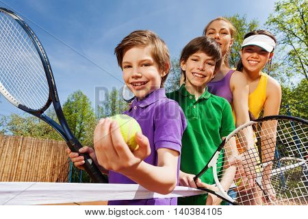 Close-up portrait of smiling active family, holding tennis rackets and ball on the court in sunny day