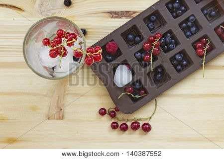 Fresh berries and drink in a glass with ice cubes. Blueberries and red currants on a wooden table background. Top view.