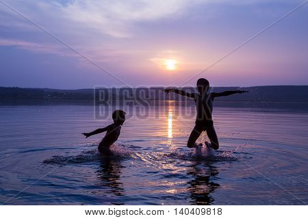 Silhouette of two boys jumping into water on sunset