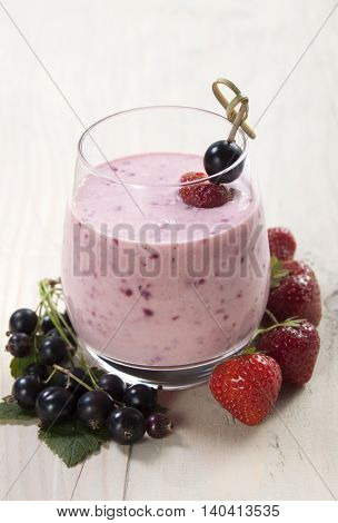 Smoothies of black currant and strawberries with yogurt on a wooden table.