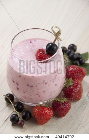 Smoothies of black currants and strawberries with yogurt on a wooden table.