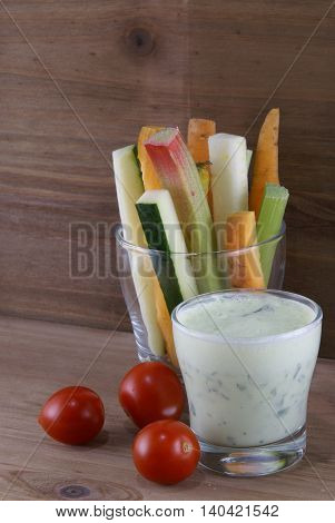 Useful summer snack: vegetables and yogurt sauce with herbs. Against the background of a rustic wooden table