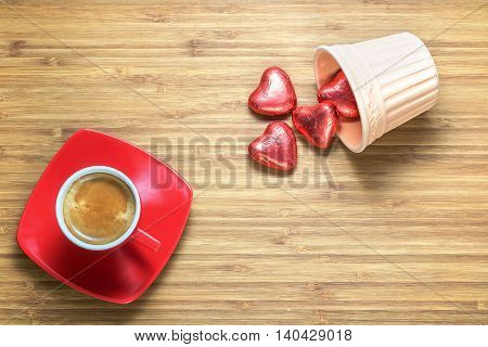 Heart shaped sweets wrapped in a bright red foil lying on a wooden texture with red cup of coffe near it. Background for romantic themes.