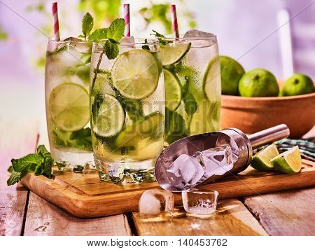 Alcohol mint sprig drink. Wooden boards three glasses with alcohol drink and ice cubes. Drink two hundred ninety-four cocktail mohito and scoop ice with straw. Country life. Outdoor. Light background.