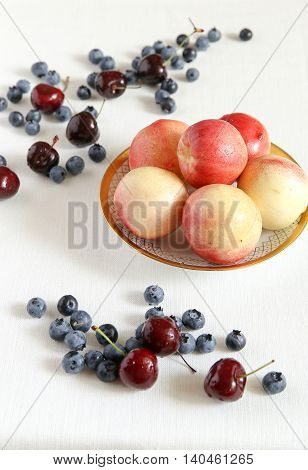 Berry mix. Peaches in a bowl cherry and bilberry. A white cloth from flax.