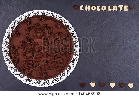 Round Chocolate cake on a slate board top view. Chocolate chocolate letters with text chocolate and copy space