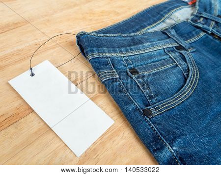 Close-up of blue jeans with deerskin label and white blank price tag on wooden texture background