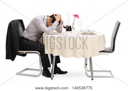 Desperate guy sitting alone at a restaurant table with his head down isolated on white background