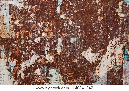 grunge ripped poster on rusty iron sheet background - texture of torn advertisement on an old rusty billboard panel