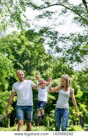 Family walking in the park in the summer. Cheerful little boy playing in the park with his parents in the summer. Dad Mom and the kids played in the park in the summer.