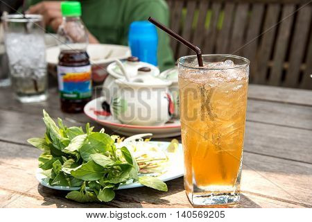 Glass tamarind juice with ice placed on wooden table.Focus top glassbackground blur and poor light.