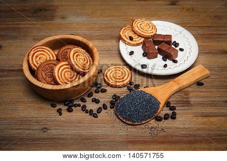 There are Cookies,Candy,Chocolate Peas,Poppy;Ceramic Plate;Tasty Sweet Food on the Wooden Background