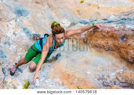 Female Athlete climbing natural rock keeping hold and hanging over deep abyss