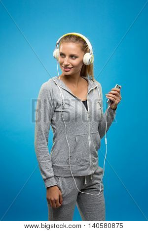 Portrait of young blonde woman in sportswear listening to music with cell phone.Studio shot. Blue background. Isolated.