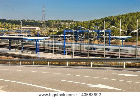 Modern high speed train departs from railway station with natural motion blur effect and beautiful landscape. Camp de Tarragona Spain. Horizontal.