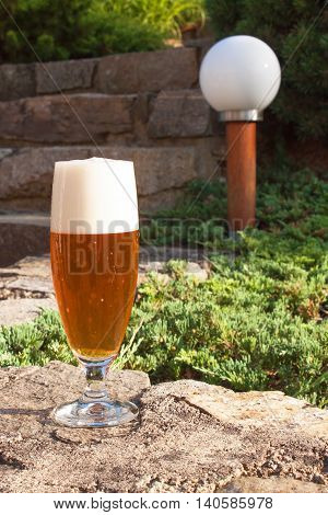 Glass of beer on a stone wall. Garden party. Beer in light of sunset. Family garden party.