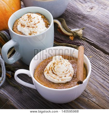 Quick meal breakfast snack in the microwave. Fragrant homemade pumpkin pie fall for five minutes in the cup portions with whipped cream and cinnamon on a wooden background. selective focus