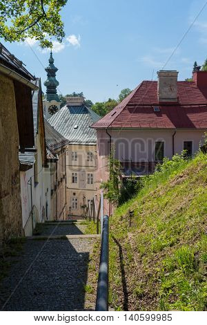 Small street on a hill in the medieval city Banska Stiavnica Slovakia. Old houses and a tower of a church. Blue summer sky with some clouds.