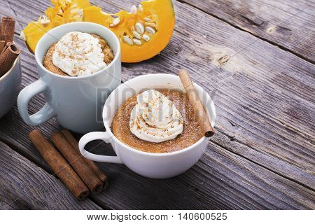 Quick meal breakfast snack in the microwave. Fragrant homemade pumpkin pie fall for five minutes in the cup portions with whipped cream and cinnamon on a wooden background. selective focus
