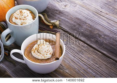 Quick meal breakfast snack in the microwave. Fragrant homemade pumpkin pie fall for five minutes in the cup portions with whipped cream and cinnamon on a wooden background. selective focus