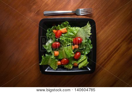 Fresh organic garden salad with Italian dressing on square black plate