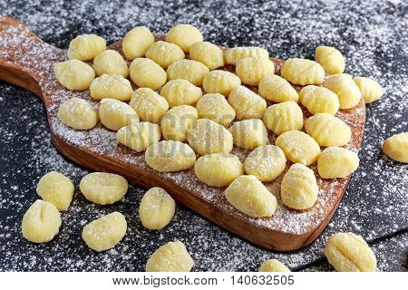 Uncooked homemade gnocchi on wooden cutting floured board.
