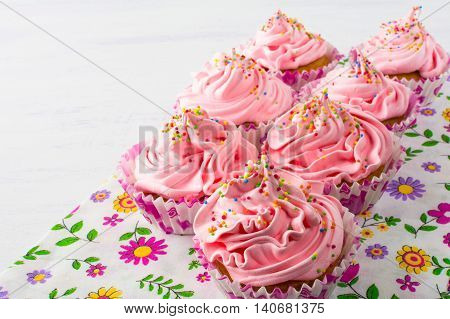 Pink cupcakes on floral napkin. Birthday cupcake with whipped cream. Homemade cupcakes served for party. Birthday background.