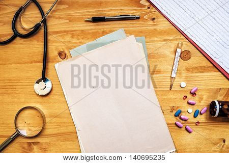 Doctor's work desk as copy space. General medical practitioner workspace with assorted office supplies such as stethoscope loupe thermometer pencil tablets and pills top view.