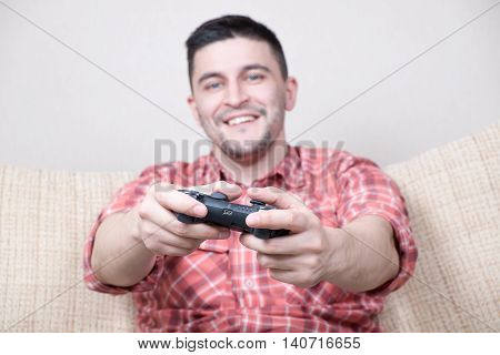 Young funny man playing video games sitting at sofa and holding remote controller