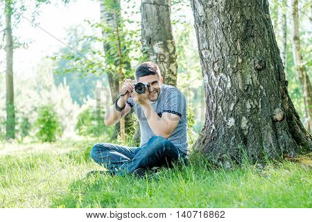 Portrait of young hipster man with camera outdoors. Young male photographer photographing nature on summer day.