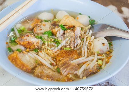 Spicy Thai Tomyum noodle with streaky pork vegetable and balls in a blue bowl.