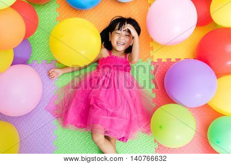 Asian Little Chinese Girl Lying On The Floor Amongst Colorful Balloons