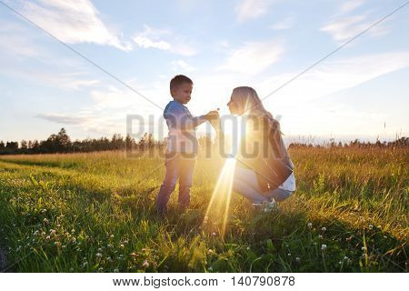 Little boy giving flower to his mom on field in evening sunlight