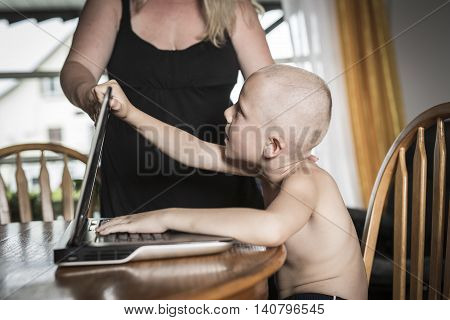 A boy with internet dependence playing with keyboard being dragged by mother from her computer