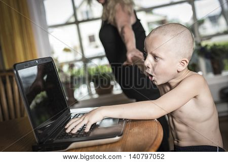 A boy with internet dependence playing with keyboard being dragged by mother from her computer