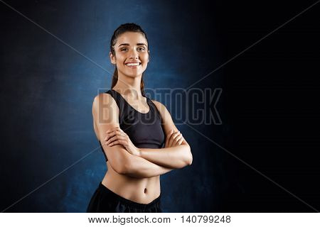 Young beautiful sportive girl posing with crossed arms over dark background. Copy space.